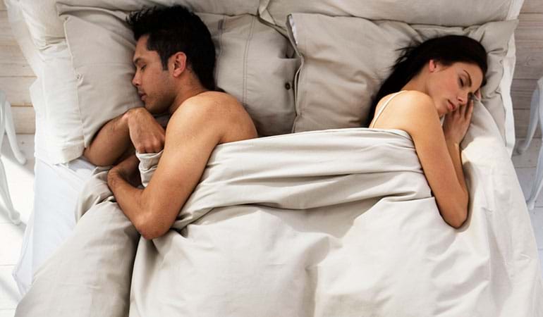 Couple in bed turned away from each other, illustrating when to go to therapy